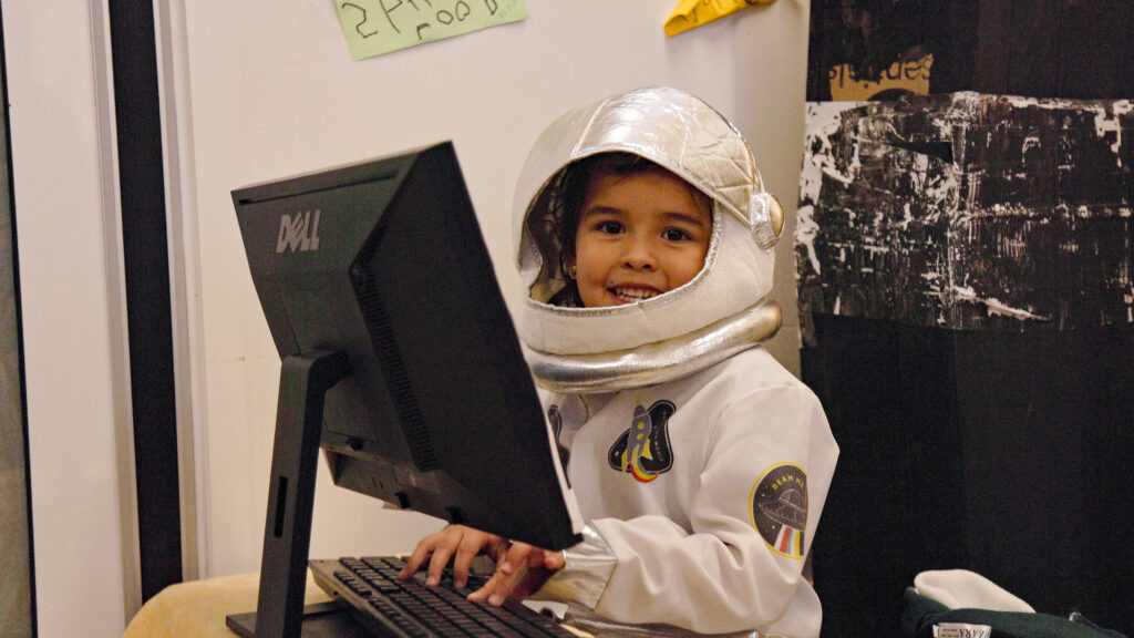 Child in astronaut suit at Sanctuary Maudsland, sitting at an old computer.