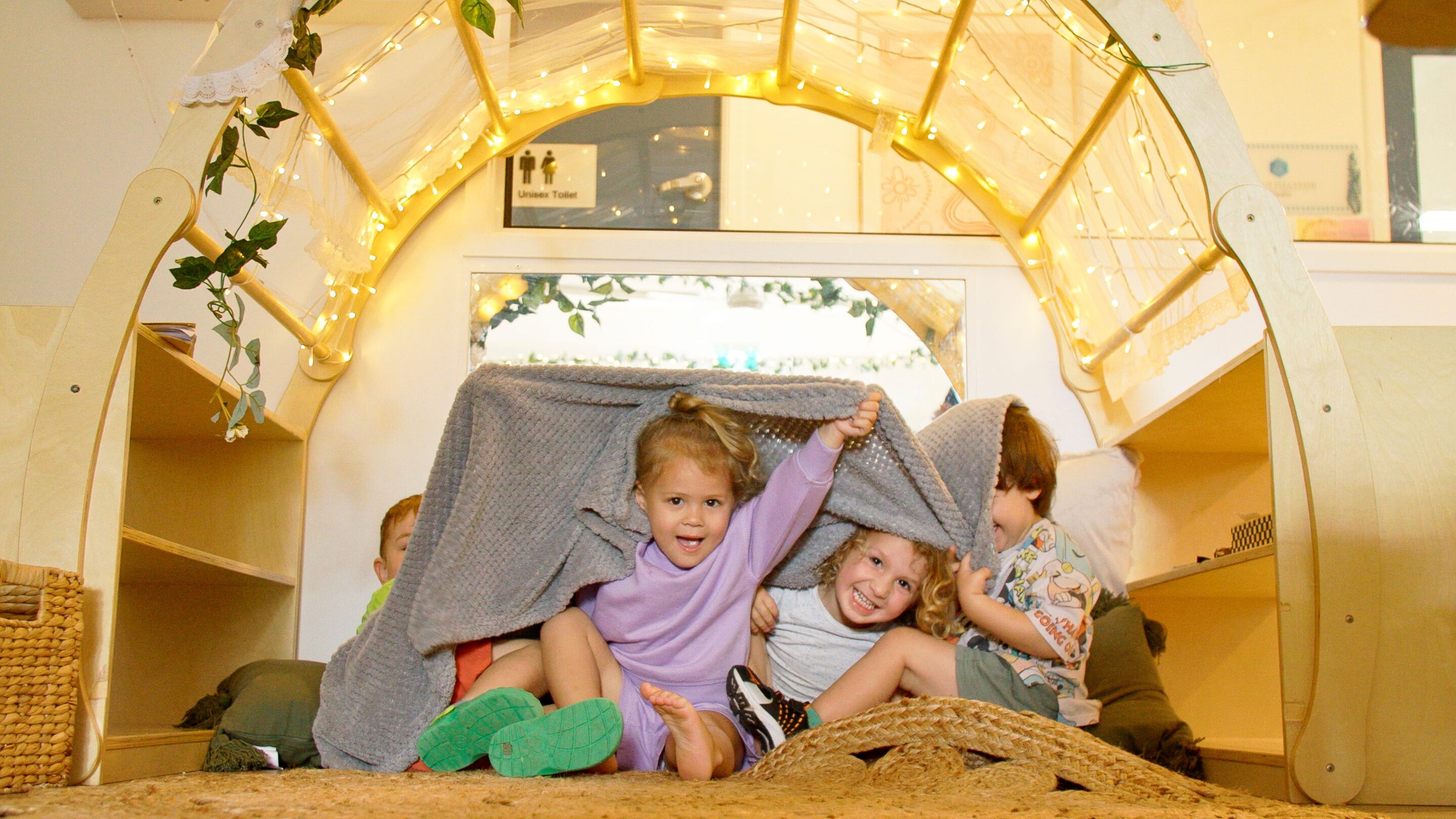 Children sitting underneath a blanket in a Sanctuary covered with fairy lights.