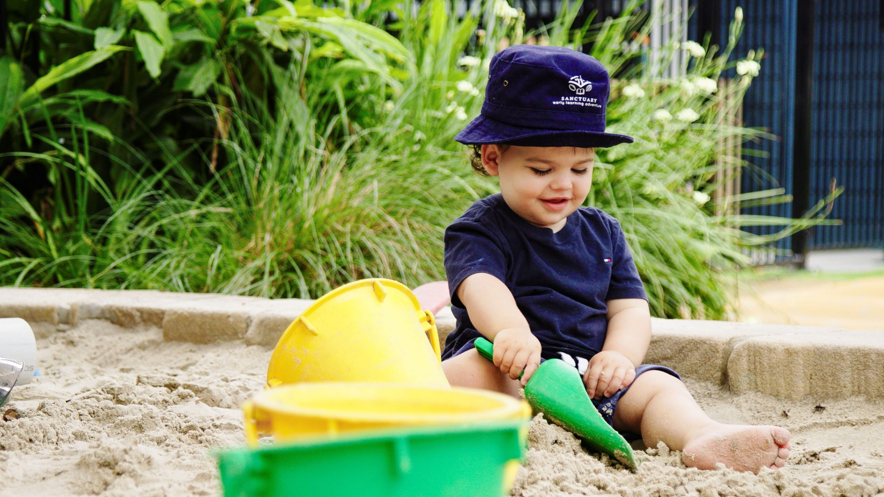 A toddler sitting in a sandpit in a child care centre.