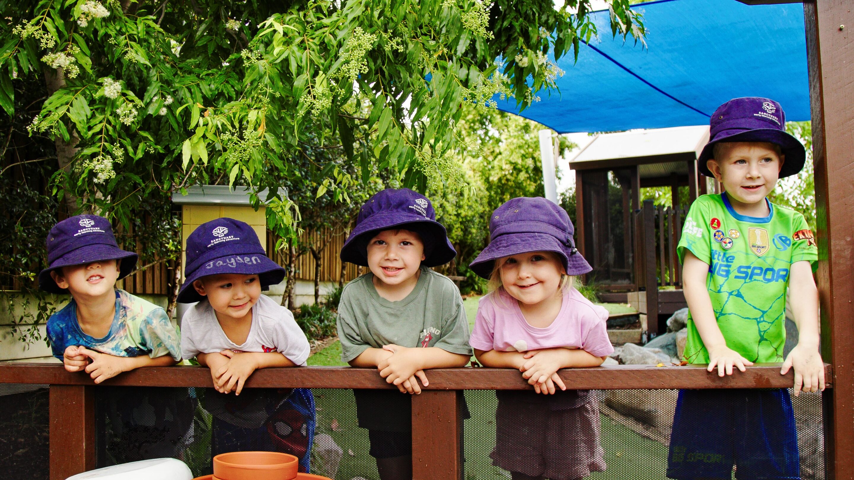 four children hanging on a post looking into a garden