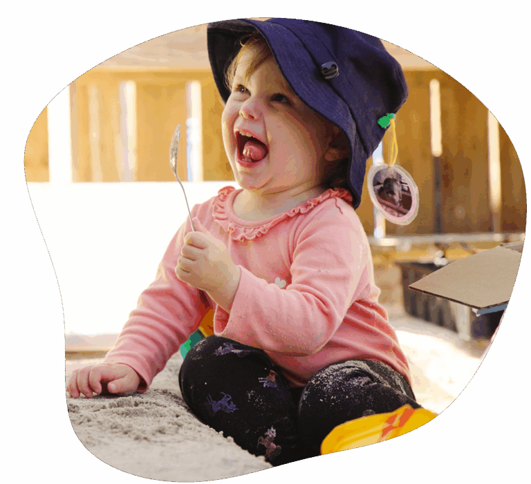 A toddler sitting in a sandpit, holding a metal spoon at a child care in Ashmore. Sanctuary Early Learning Adventure