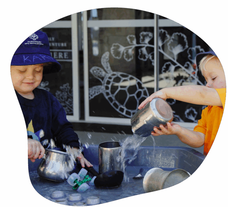 Two children playing in a tray of ice and water at the Ashmore child care centre - Sanctuary Ashmore.